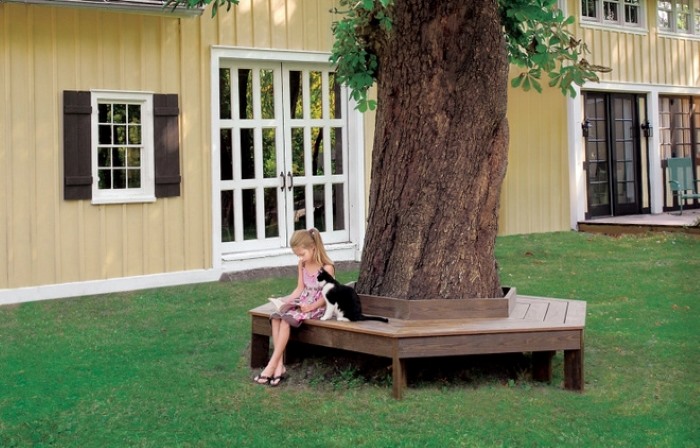 Hình ảnh cô bé đang chơi dưới gốc cây được trang trí bằng ghế ngồi.